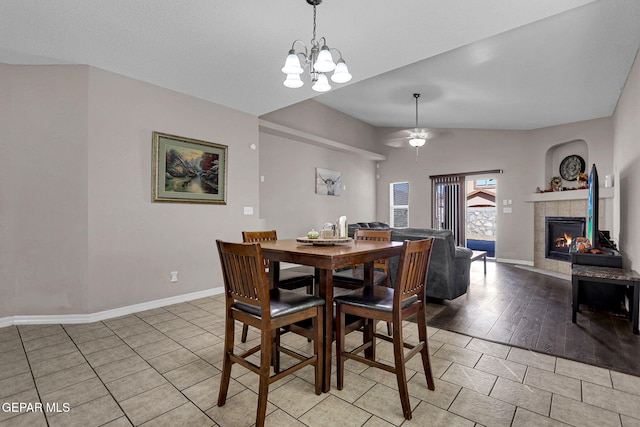 dining room with light hardwood / wood-style flooring, a tiled fireplace, lofted ceiling, and ceiling fan with notable chandelier