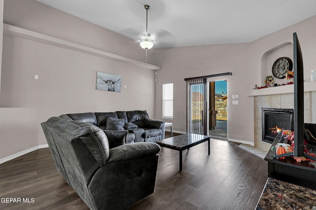 living room featuring a tiled fireplace, vaulted ceiling, dark hardwood / wood-style flooring, and ceiling fan