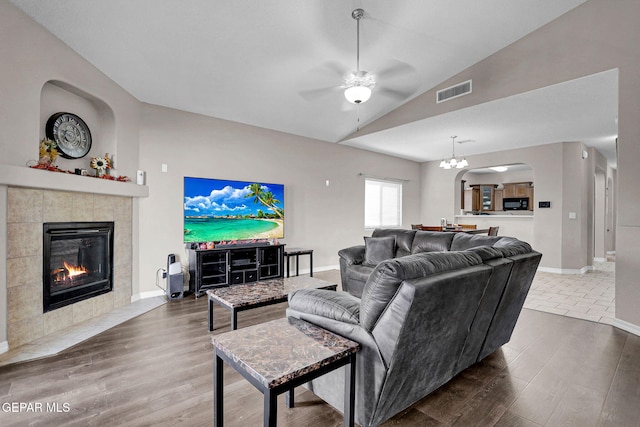 living room featuring dark hardwood / wood-style floors, a tile fireplace, ceiling fan with notable chandelier, and vaulted ceiling