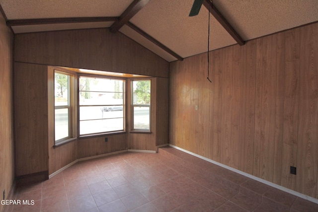 unfurnished room with lofted ceiling with beams, ceiling fan, wood walls, and a textured ceiling