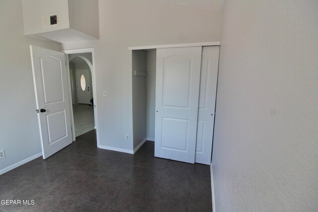 unfurnished bedroom with a towering ceiling, a closet, and dark tile patterned flooring