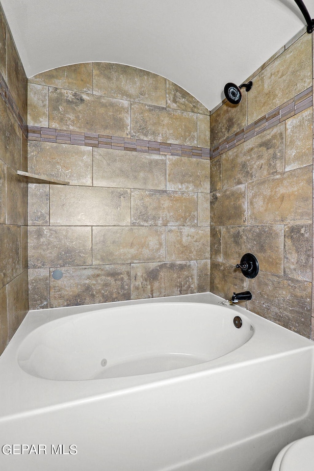 bathroom featuring vaulted ceiling, toilet, and tiled shower / bath