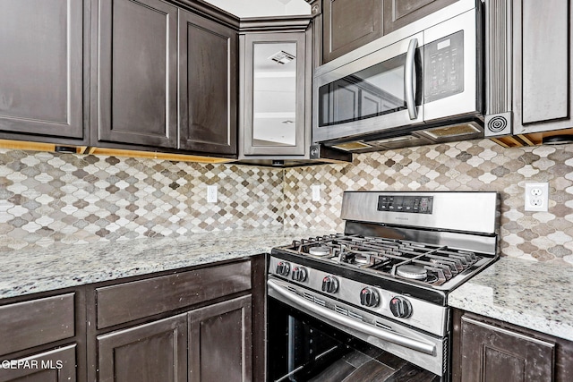 kitchen with dark brown cabinets, appliances with stainless steel finishes, light stone counters, and tasteful backsplash