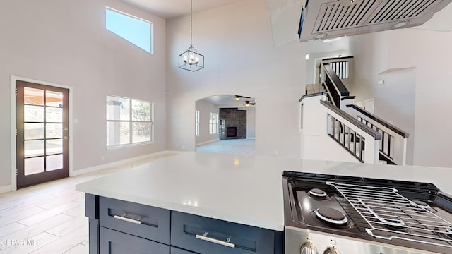 kitchen featuring a tiled fireplace, hanging light fixtures, a towering ceiling, light hardwood / wood-style flooring, and blue cabinets