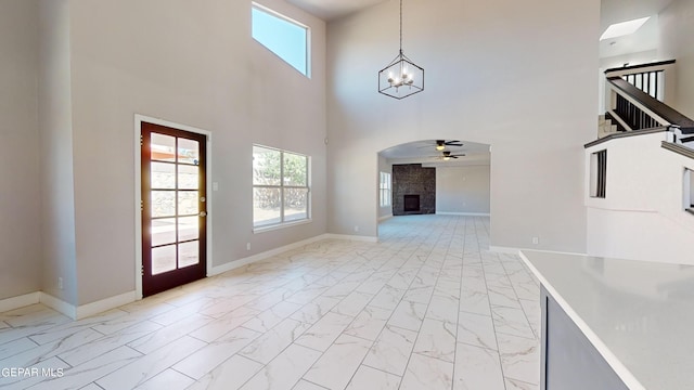 unfurnished living room featuring ceiling fan with notable chandelier, a fireplace, a wealth of natural light, and a towering ceiling