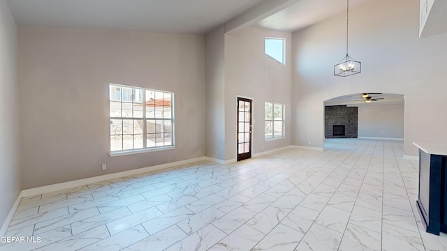 unfurnished living room with ceiling fan with notable chandelier, high vaulted ceiling, a fireplace, and a healthy amount of sunlight