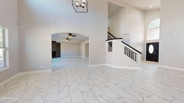 interior space with a towering ceiling, ceiling fan with notable chandelier, and a tile fireplace