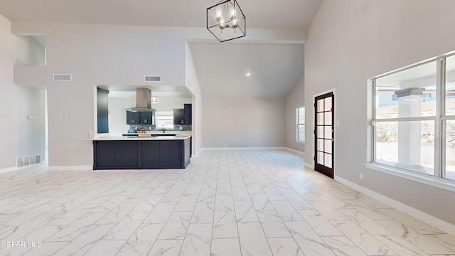 kitchen with high vaulted ceiling, kitchen peninsula, hanging light fixtures, an inviting chandelier, and island exhaust hood