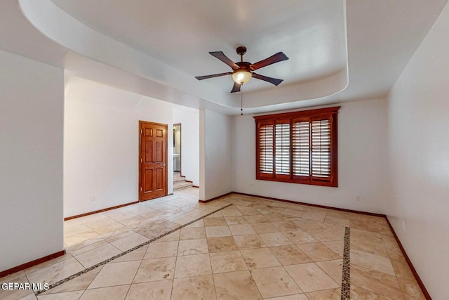 empty room featuring ceiling fan, light tile patterned flooring, and a raised ceiling