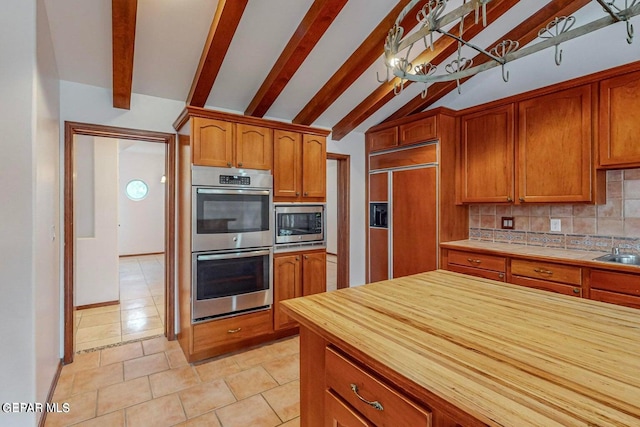 kitchen with vaulted ceiling with beams, light tile patterned floors, built in appliances, and backsplash