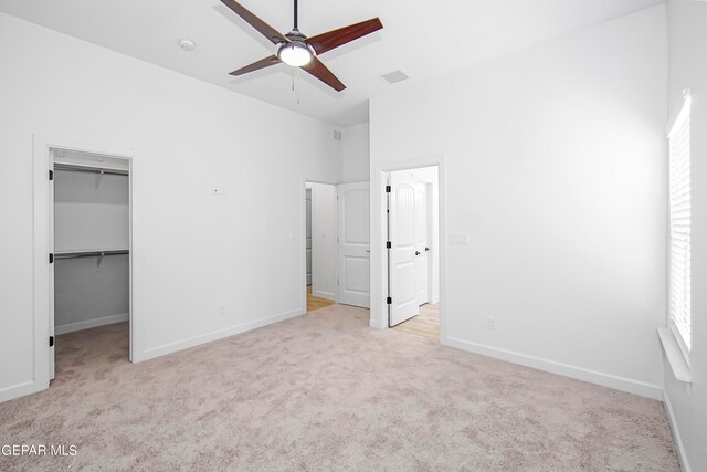 unfurnished bedroom featuring light carpet, a walk in closet, a closet, and ceiling fan