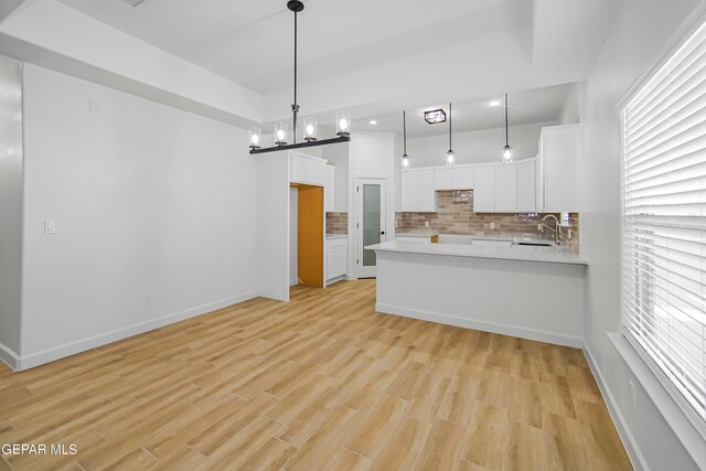 kitchen featuring white cabinets, backsplash, pendant lighting, light hardwood / wood-style floors, and a notable chandelier