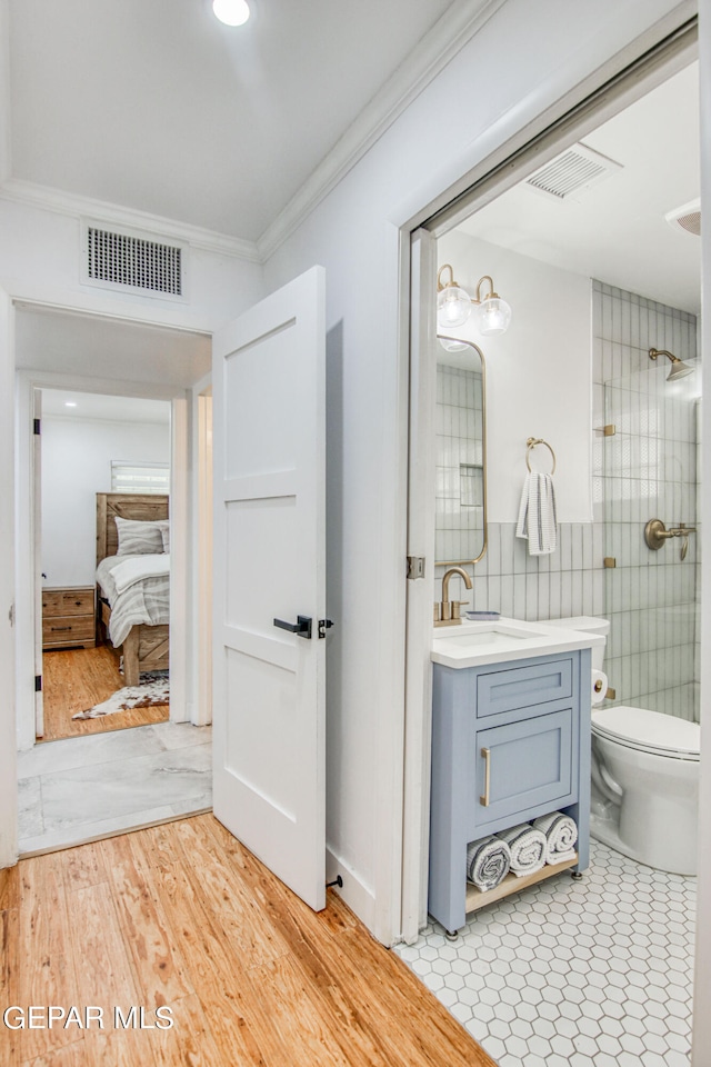 bathroom with a tile shower, toilet, vanity, crown molding, and hardwood / wood-style flooring