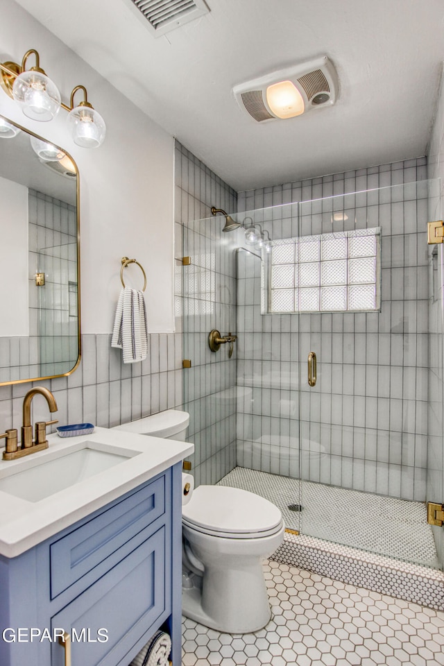 bathroom with tile walls, toilet, a shower with shower door, vanity, and tile patterned flooring