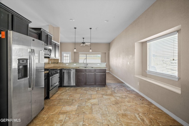 kitchen featuring hanging light fixtures, stainless steel appliances, sink, light stone countertops, and ceiling fan