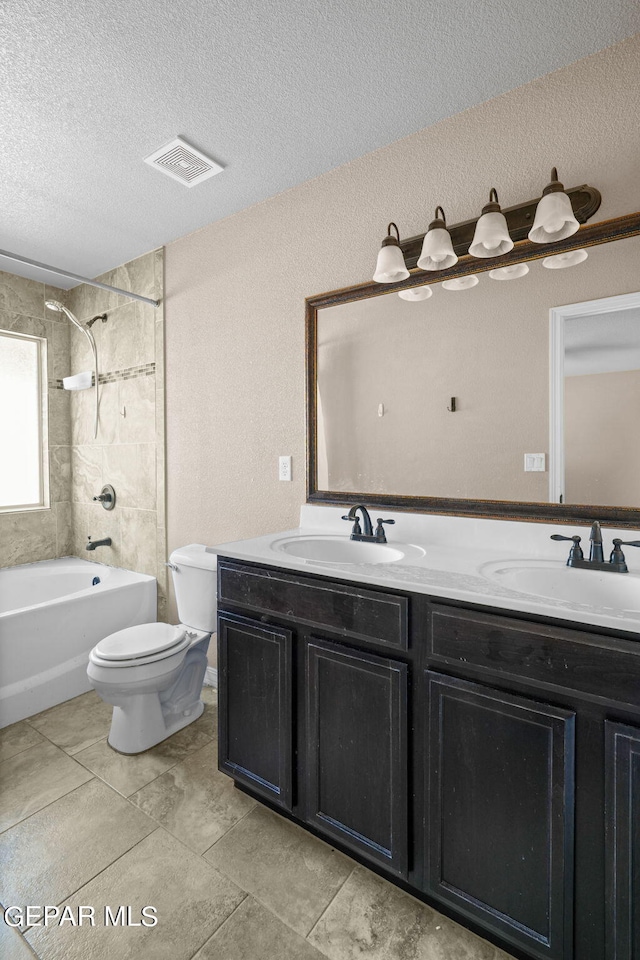 full bathroom featuring vanity, toilet, tiled shower / bath combo, and a textured ceiling