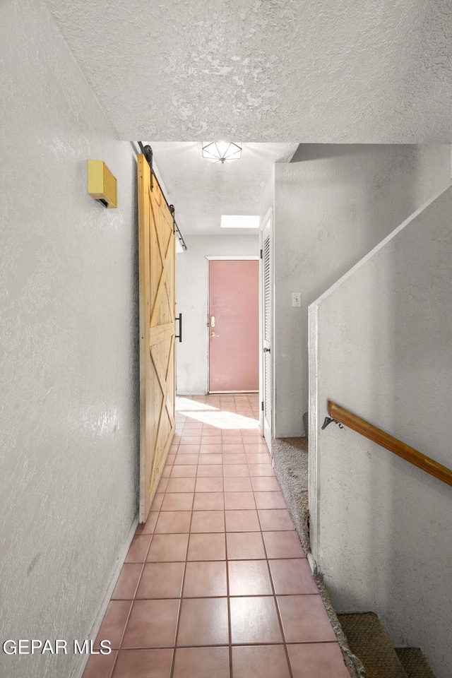 hallway with a barn door, a textured ceiling, and light tile patterned floors