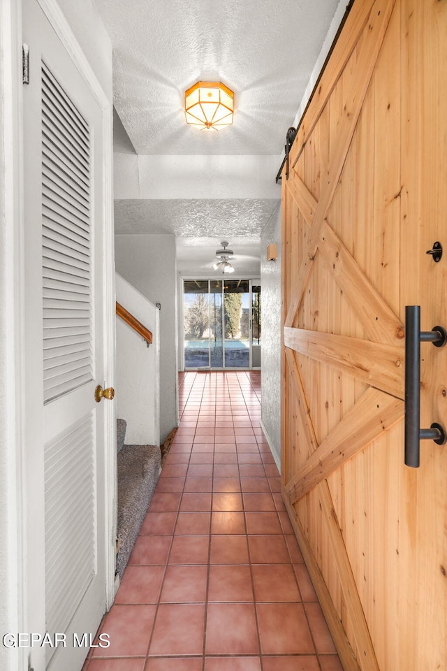 hallway featuring tile patterned floors, a textured ceiling, and a barn door