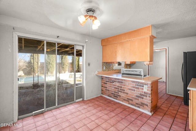kitchen with kitchen peninsula, decorative backsplash, ceiling fan, black fridge, and light tile patterned flooring
