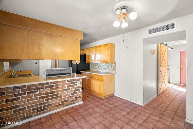 kitchen featuring kitchen peninsula, decorative backsplash, black fridge, a barn door, and sink