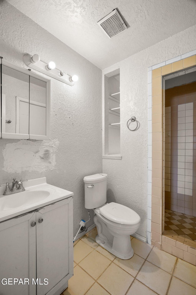 bathroom featuring a tile shower, a textured ceiling, toilet, vanity, and tile patterned floors