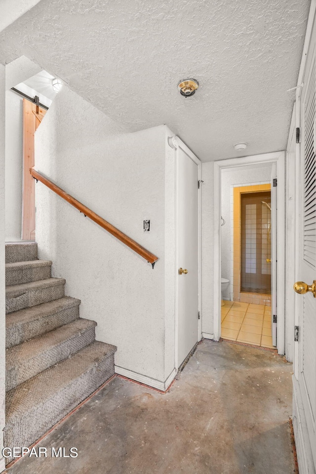 staircase featuring a barn door, a textured ceiling, and concrete floors