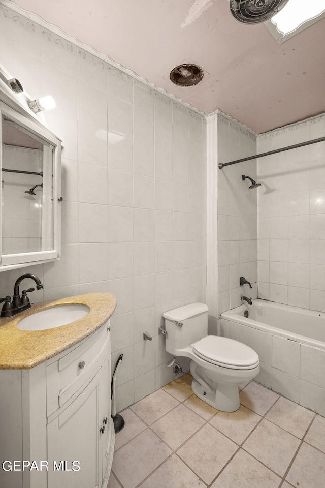 full bathroom featuring toilet, tile patterned floors, tile walls, vanity, and tiled shower / bath combo