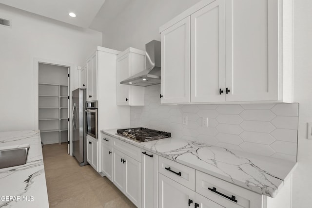 kitchen with decorative backsplash, light stone counters, white cabinetry, wall chimney exhaust hood, and stainless steel appliances