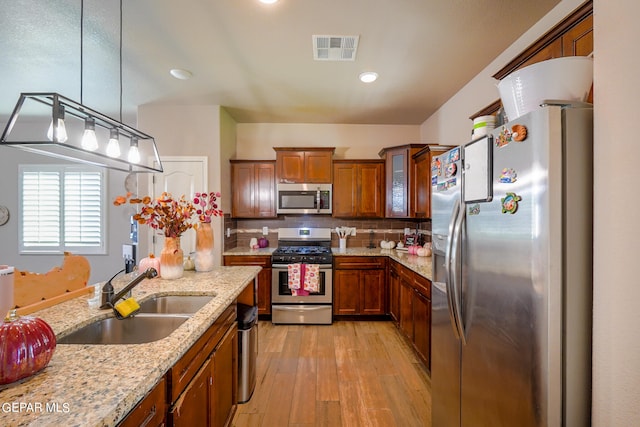 kitchen with hanging light fixtures, light stone counters, appliances with stainless steel finishes, light hardwood / wood-style floors, and sink