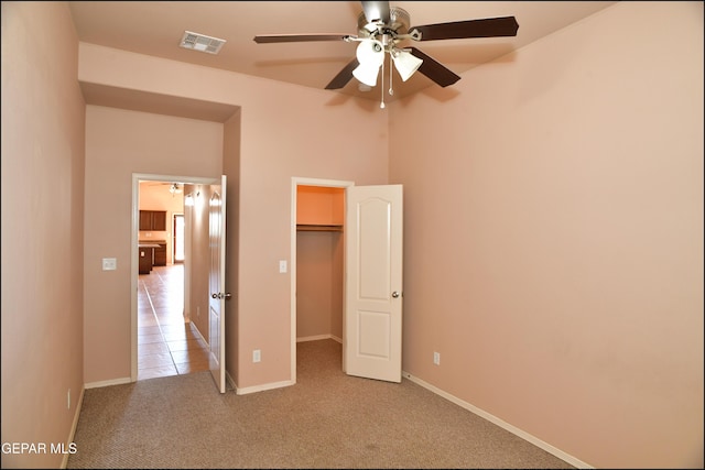 unfurnished bedroom featuring a closet, light colored carpet, a spacious closet, and ceiling fan