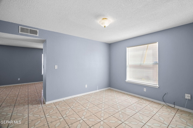 spare room with a textured ceiling and light tile patterned flooring