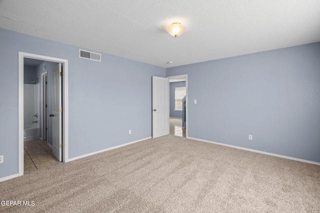 unfurnished bedroom with connected bathroom, light carpet, and a textured ceiling