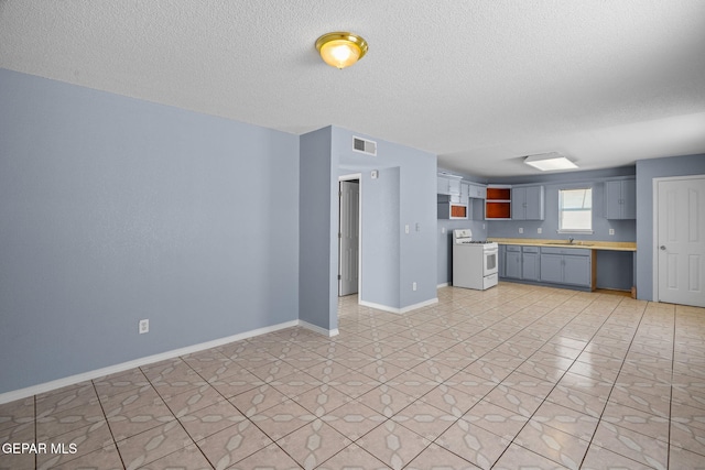 kitchen featuring gray cabinetry, white range oven, sink, light tile patterned floors, and a textured ceiling