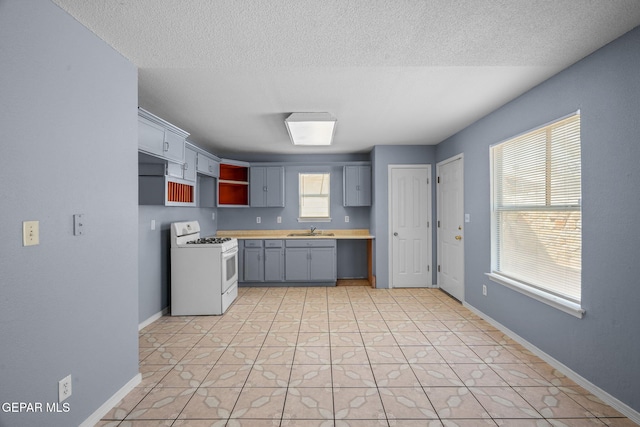 kitchen with white range with gas cooktop, sink, plenty of natural light, and gray cabinetry