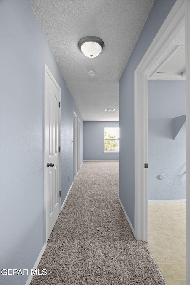 hallway featuring a textured ceiling and light colored carpet