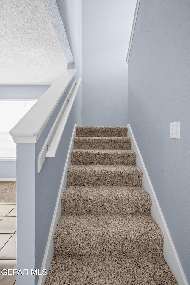 staircase with a textured ceiling and tile patterned floors