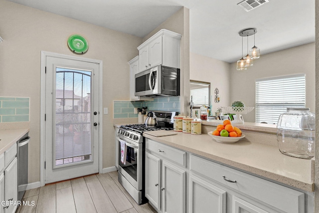 kitchen featuring hanging light fixtures, appliances with stainless steel finishes, a wealth of natural light, and white cabinets