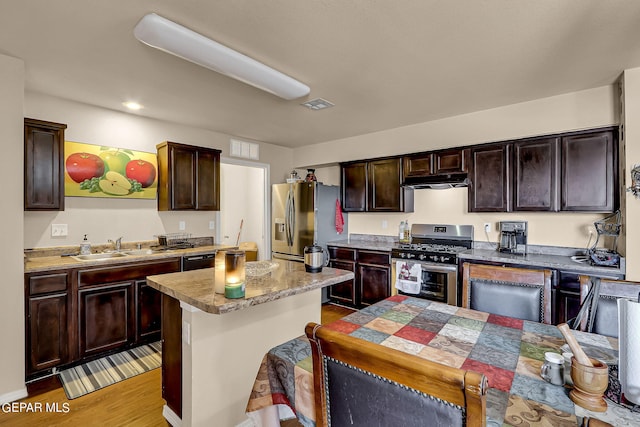 kitchen with appliances with stainless steel finishes, a breakfast bar, light hardwood / wood-style flooring, dark brown cabinetry, and a center island