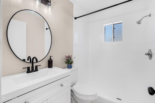 bathroom featuring vanity, a tile shower, and toilet