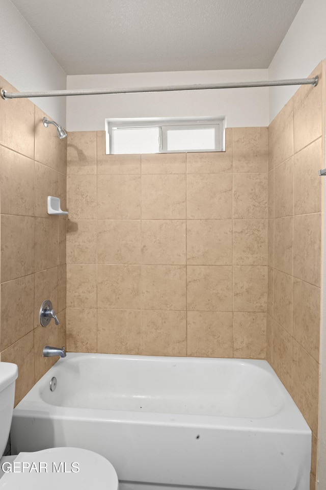 bathroom featuring tiled shower / bath, toilet, and a textured ceiling