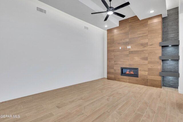 unfurnished living room featuring wood walls, light hardwood / wood-style flooring, a large fireplace, and ceiling fan