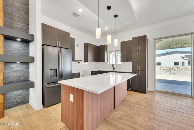 kitchen featuring light wood-type flooring, a kitchen island, backsplash, hanging light fixtures, and stainless steel fridge with ice dispenser