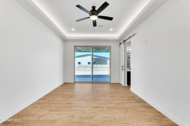 spare room featuring ceiling fan, a tray ceiling, light hardwood / wood-style flooring, and a barn door