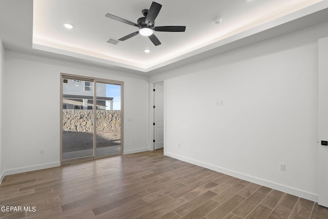 empty room with ceiling fan, hardwood / wood-style flooring, and a raised ceiling