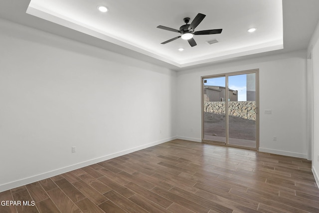 unfurnished room featuring ceiling fan, a raised ceiling, and dark hardwood / wood-style floors