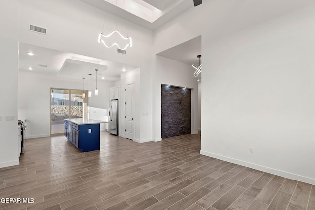 kitchen featuring a towering ceiling, light wood-type flooring, a kitchen island, stainless steel fridge, and blue cabinetry