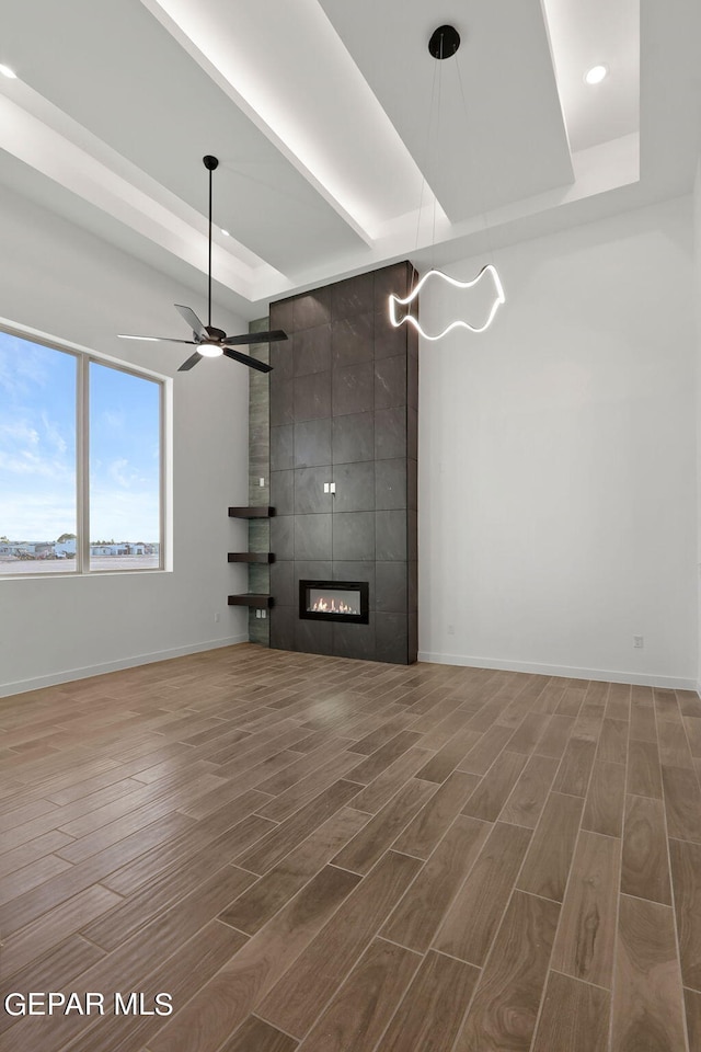 unfurnished living room with a tiled fireplace, hardwood / wood-style flooring, and a tray ceiling