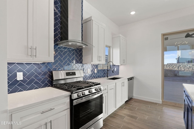 kitchen featuring appliances with stainless steel finishes, sink, light hardwood / wood-style floors, wall chimney exhaust hood, and white cabinets