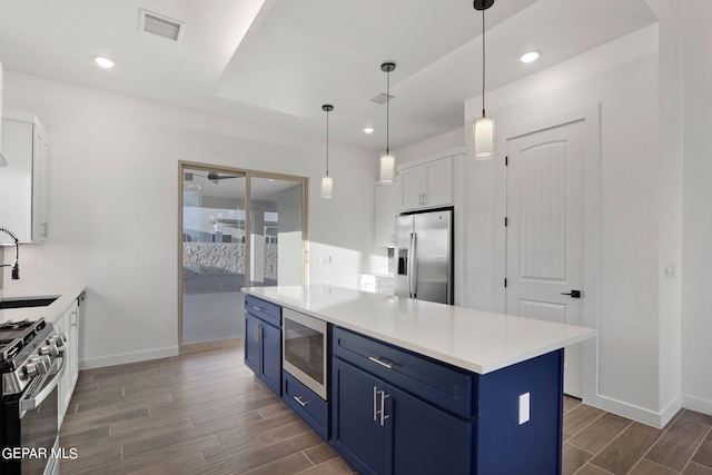 kitchen featuring appliances with stainless steel finishes, dark hardwood / wood-style flooring, blue cabinets, decorative light fixtures, and white cabinets