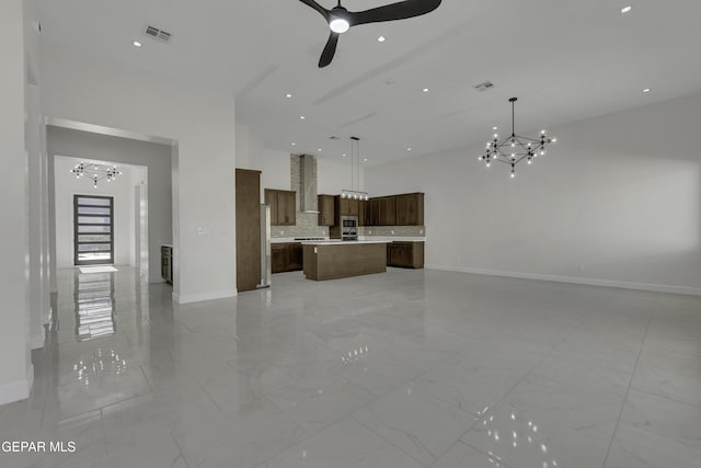 unfurnished living room featuring ceiling fan with notable chandelier and a towering ceiling